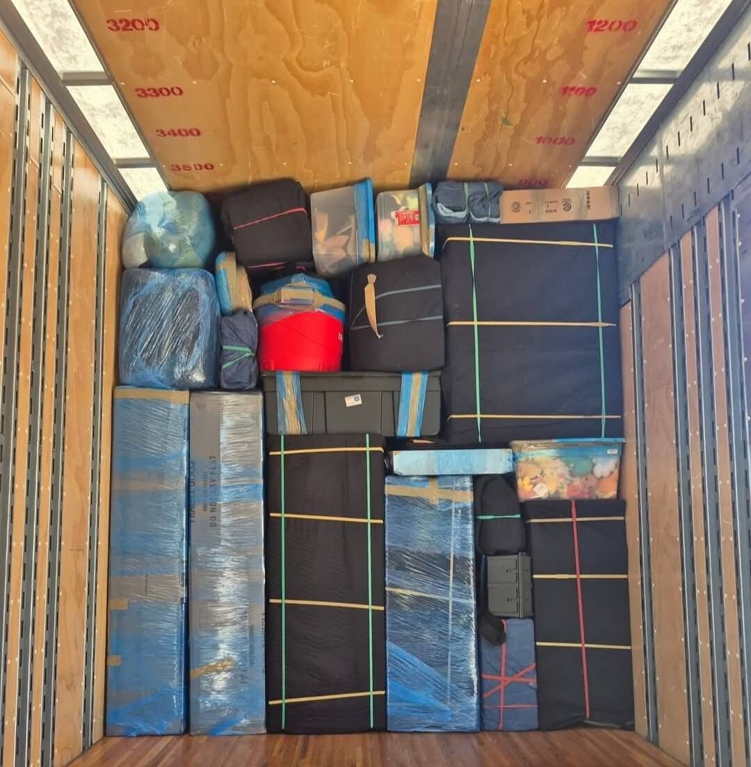 Tight truck loading with blue moving-blanket-wrapped furniture and plastic-covered mattresses — Dallas, TX