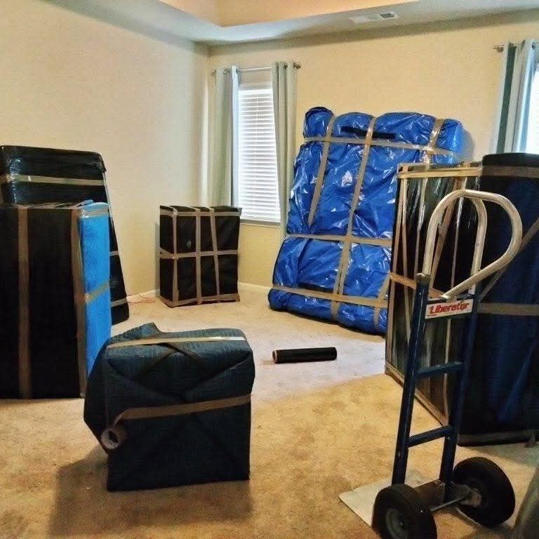 Bedroom with plastic-wrapped and blue blanket-wrapped furniture staged for move with Liberator appliance dolly — One World Van Lines Irving, TX DFW Metroplex professional movers