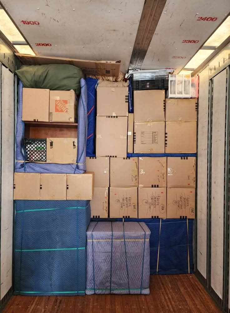 Moving truck interior showing blue blanket-wrapped furniture and stacked household boxes secured with straps — One World Van Lines Denton, TX DFW Metroplex professional movers