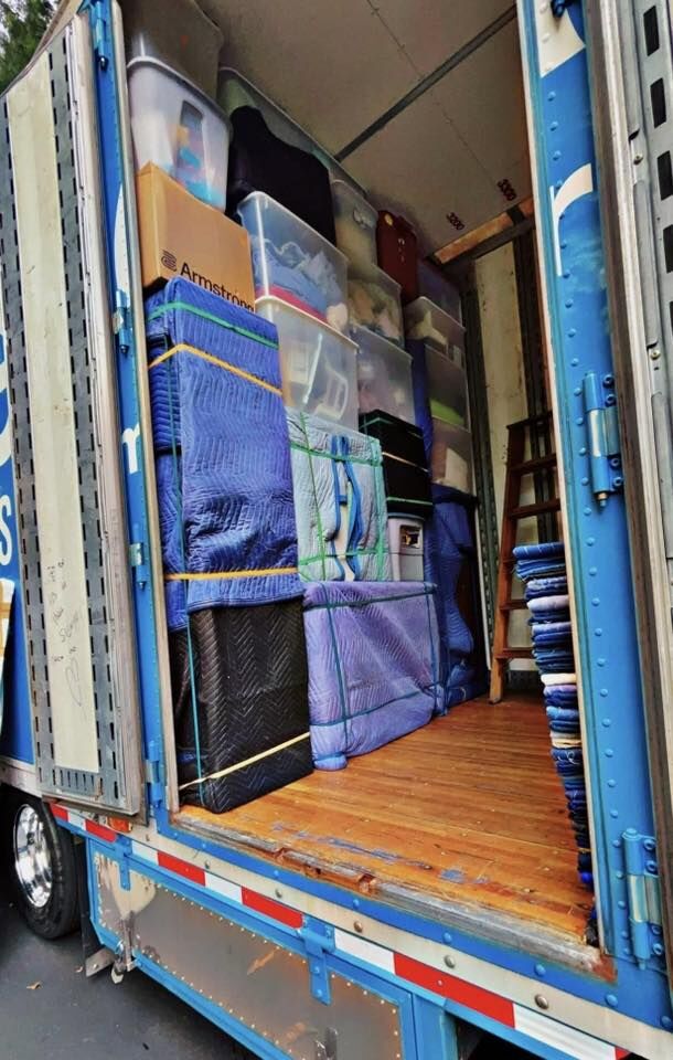 Blue moving truck exterior open doors showing wrapped furniture, plastic tubs and Armstrong flooring box loaded inside — One World Van Lines Bastrop, TX Greater Austin professional movers
