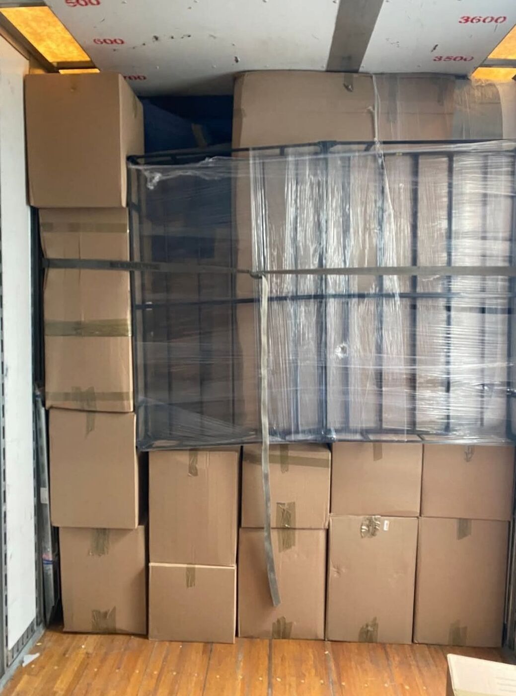 Cardboard boxes stacked ceiling to floor alongside plastic-wrapped metal shelving unit in moving truck — One World Van Lines Bedford, TX DFW Metroplex