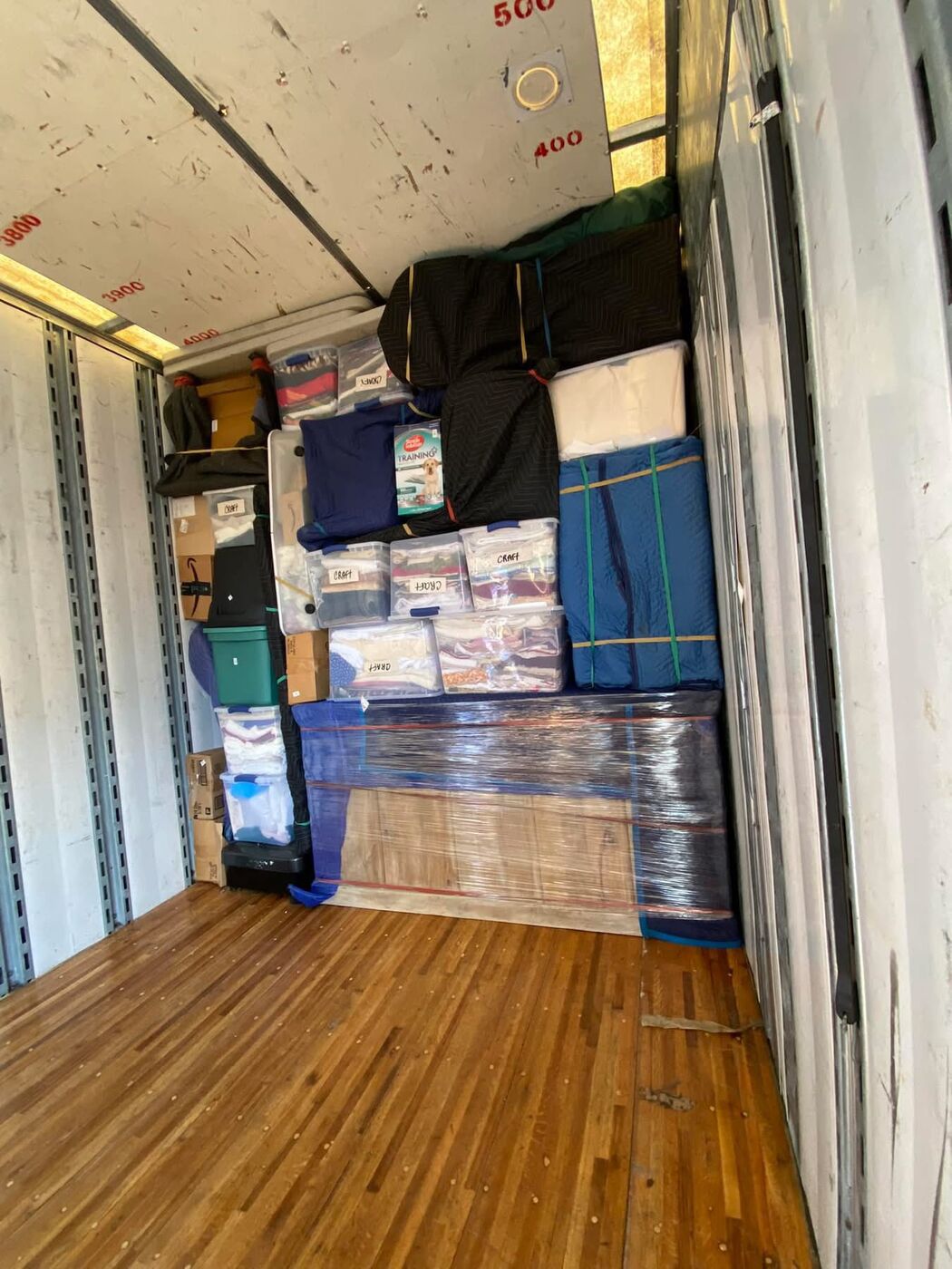 Moving truck interior with labeled CRAFT plastic tubs, plastic-shrink-wrapped hardwood flooring, blanket-wrapped furniture — One World Van Lines Buda, TX Greater Austin movers
