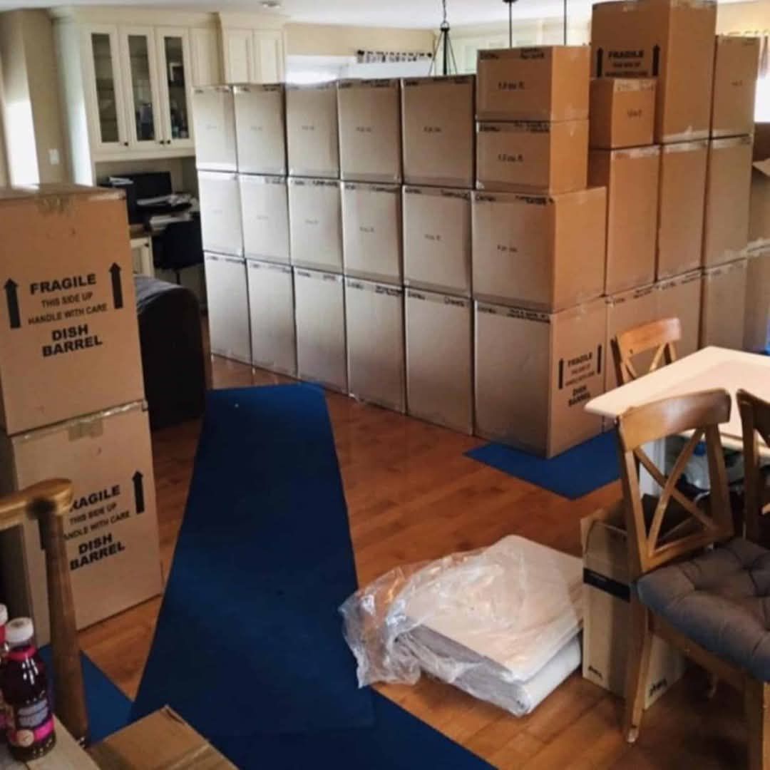 Full kitchen and dining room staged for move day with dish barrel fragile boxes stacked floor-to-ceiling and blue carpet runner protecting hardwood floors — One World Van Lines Frisco, TX DFW Metroplex professional movers
