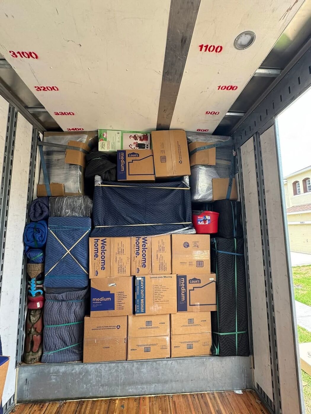 Moving truck loaded with Lowe's Welcome Home boxes, rolled area rugs, navy blanket-wrapped furniture and red bucket — One World Van Lines Little Elm, TX DFW Metroplex movers