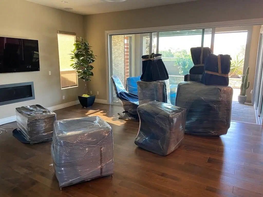 Luxury modern home living room with plastic-wrapped sofas and accent chairs staged for move with slider door view — One World Van Lines Westlake Hills, TX Greater Austin high-value movers