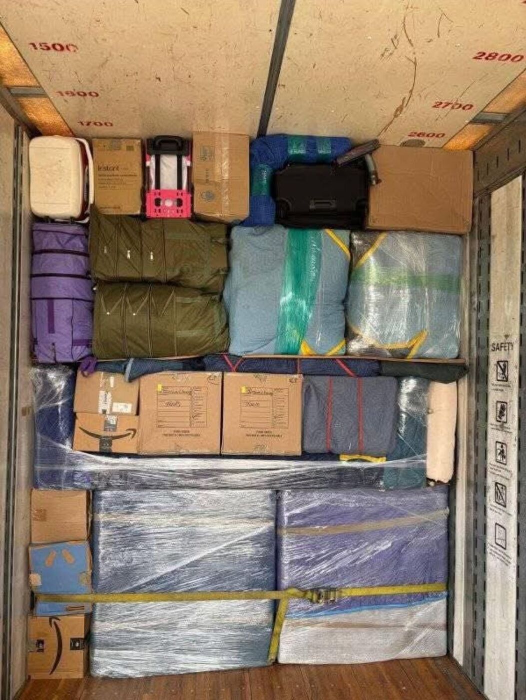 Organized moving truck with suitcases, plastic-wrapped blankets, Amazon and wardrobe boxes with ratchet straps — One World Van Lines McKinney, TX DFW Metroplex