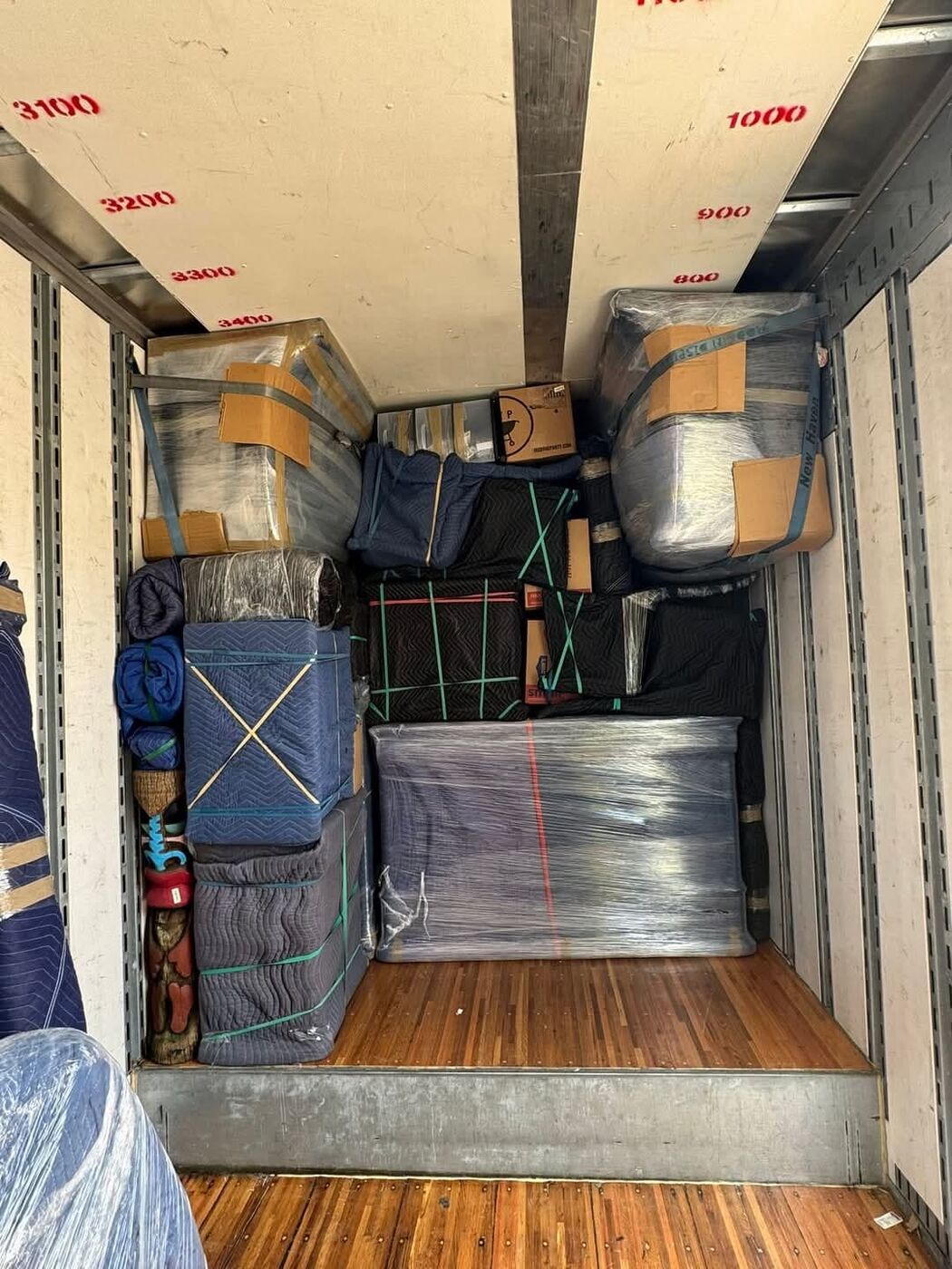 Moving truck fully stacked with plastic-wrapped and navy blanket-wrapped furniture secured with straps — One World Van Lines San Marcos, TX Greater Austin professional movers