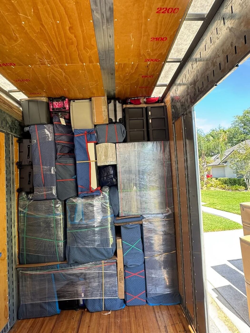 Moving truck rear with plastic-wrapped furniture, blue blanket-wrapped items, luggage and suitcases — One World Van Lines Leander, TX Greater Austin movers