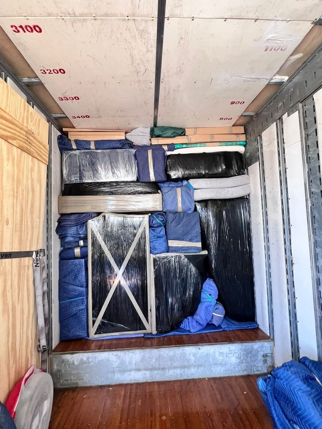 Plastic-wrapped mattresses, blue blanket-wrapped furniture and wooden door panel packed in moving truck — One World Van Lines Grand Prairie, TX DFW movers