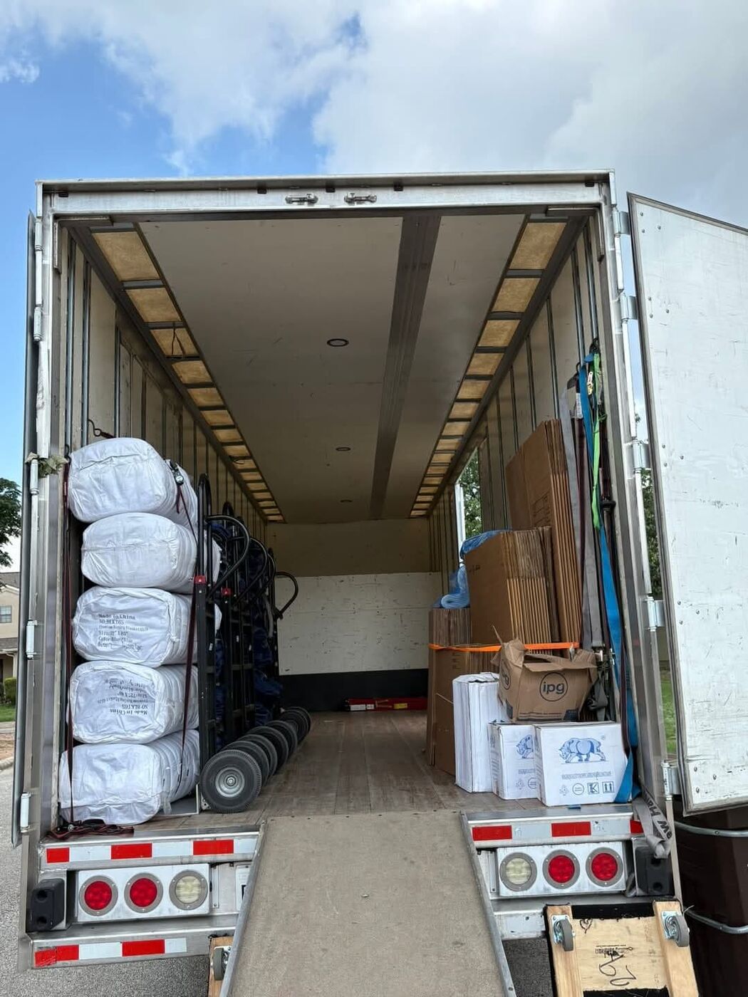 Large moving truck with ramp deployed, stacked mattress bags, dolly and IPG packing supplies ready to load — One World Van Lines Pflugerville, TX Greater Austin professional movers