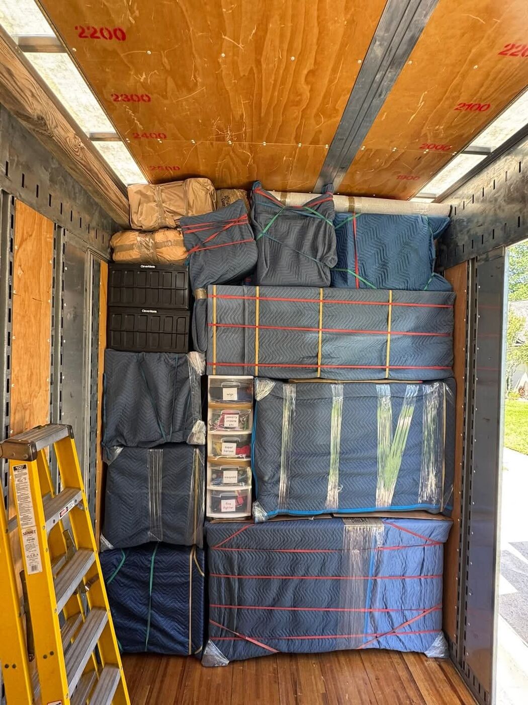 Moving truck packed wall-to-wall with blue blanket-wrapped furniture secured with bungee cords at suburban neighborhood — One World Van Lines Round Rock, Austin TX