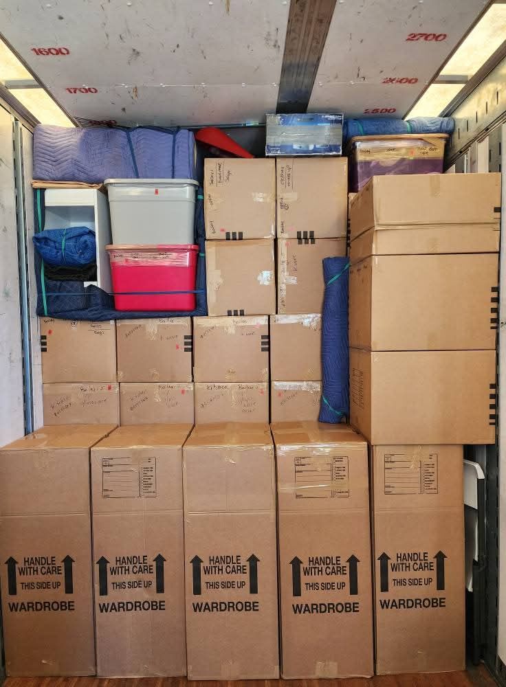 Moving truck fully loaded with wardrobe Handle-With-Care boxes, pink and gray storage tubs and hand-labeled household boxes — One World Van Lines New Braunfels, TX Greater Austin movers