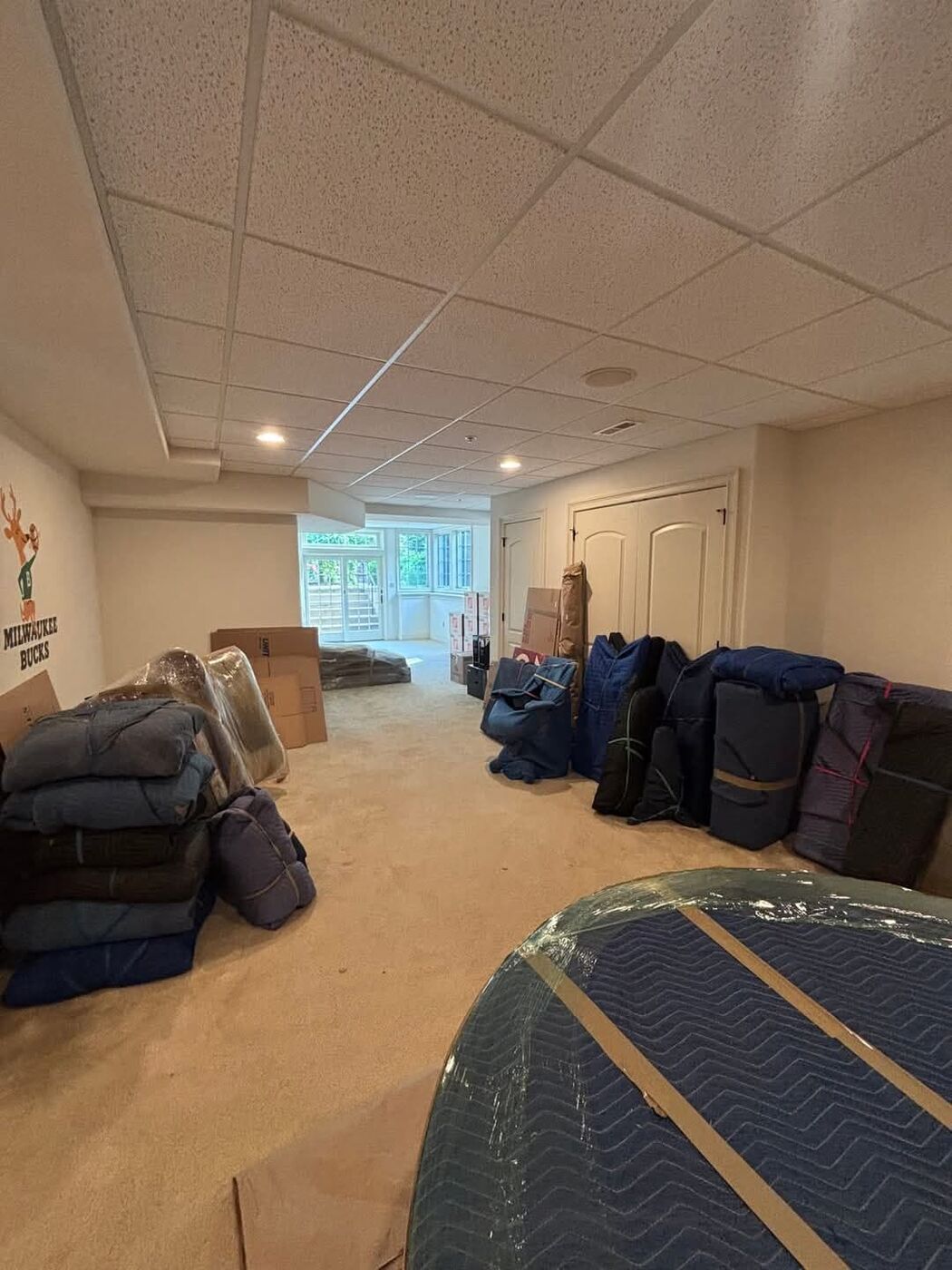 Blue blanket-wrapped furniture pieces and packed boxes staged in basement recreation room before move — One World Van Lines Prosper, TX DFW Metroplex